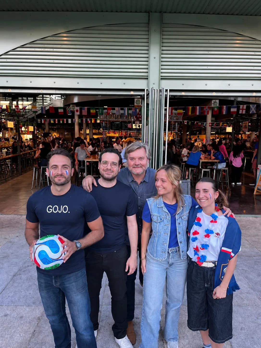 Devant la Halle Biltoki de Rueil-Malmaison grande ouverte, le soir du premier match des Bleus : cinq personnes souriantes, des drapeaux tricolores peints sur les joues, l’une avec un ballon et un t-shirt GOJO. Derrière elles, la Halle pleine, sous les fanions des pays.
